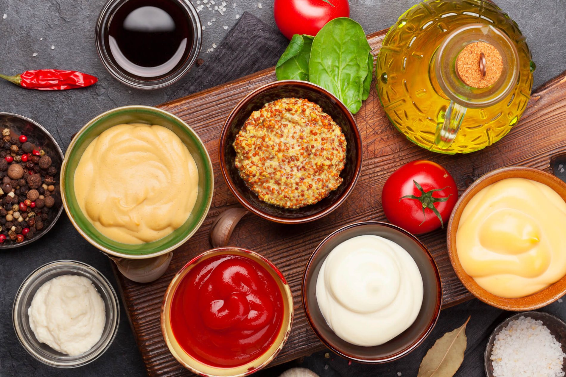 Ciotole con salse e condimenti assortiti, dalle ricette classiche alle varianti etniche, accompagnate da spezie, pomodori e olio