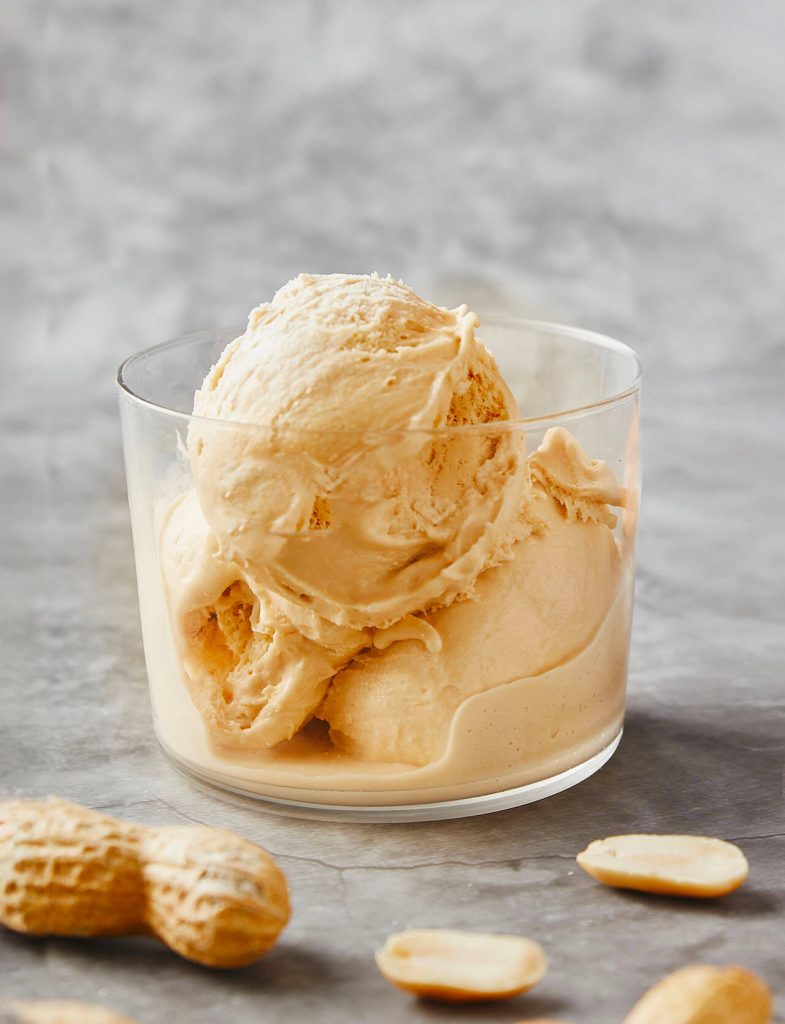 Gelati proteici: coppetta di gelato proteico al burro d’arachidi con arachidi attorno