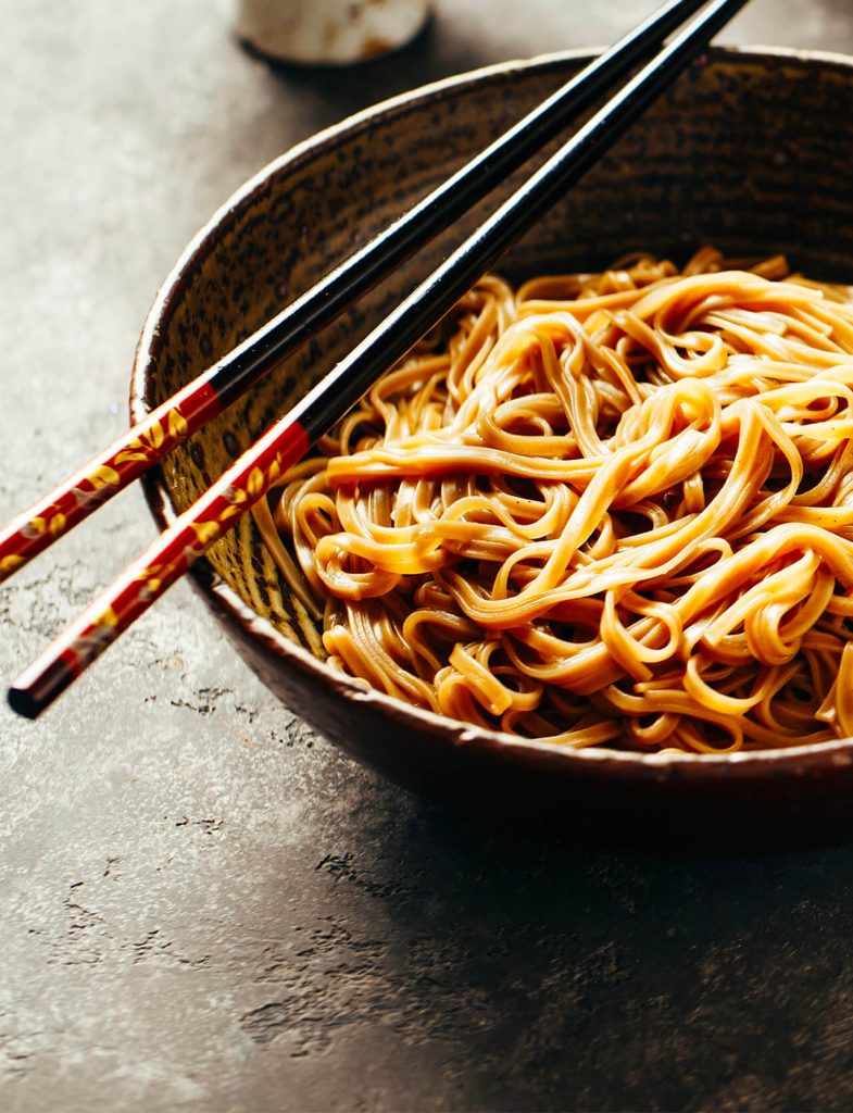 Noodle etnici serviti in ciotola con bacchette, tipici della cucina asiatica.