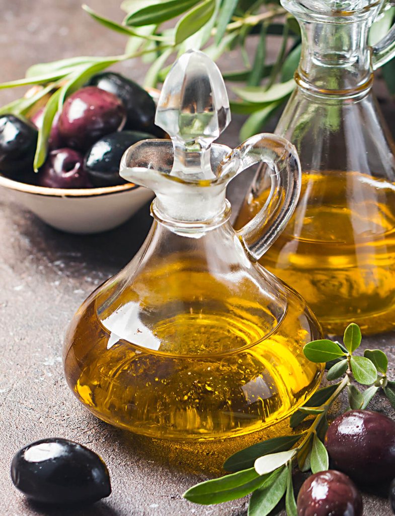 Bottiglie di vetro con olio extravergine d’oliva accanto a rami di ulivo e olive fresche.