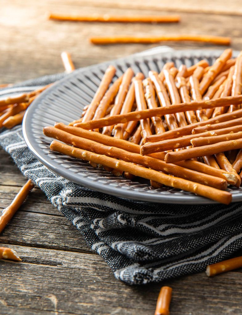 Mix di salatini croccanti in ciotola di legno, con forme diverse come mini pretzel e crackers salati, perfetti per snack e aperitivi.