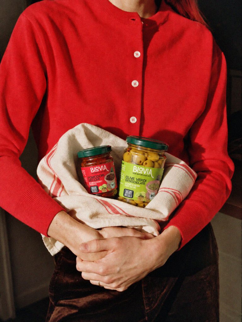 Jars of BIOVIA organic sun-dried tomatoes and pitted green olives wrapped in a tea towel