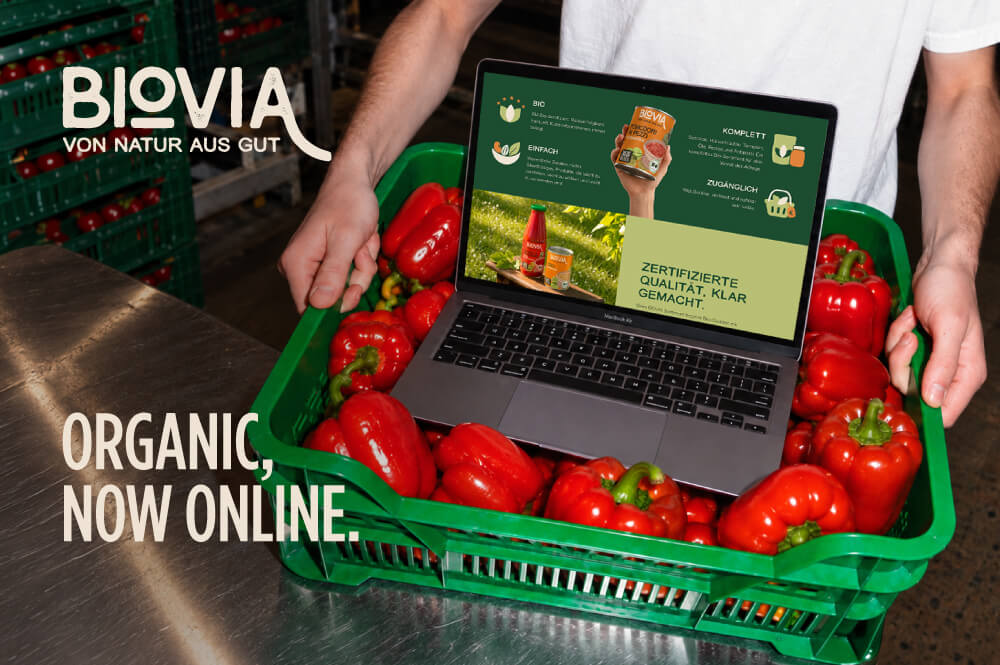 Laptop con il sito BIOVIA in una cassetta di peperoni rossi, logo del brand e claim «Il biologico, ora online»