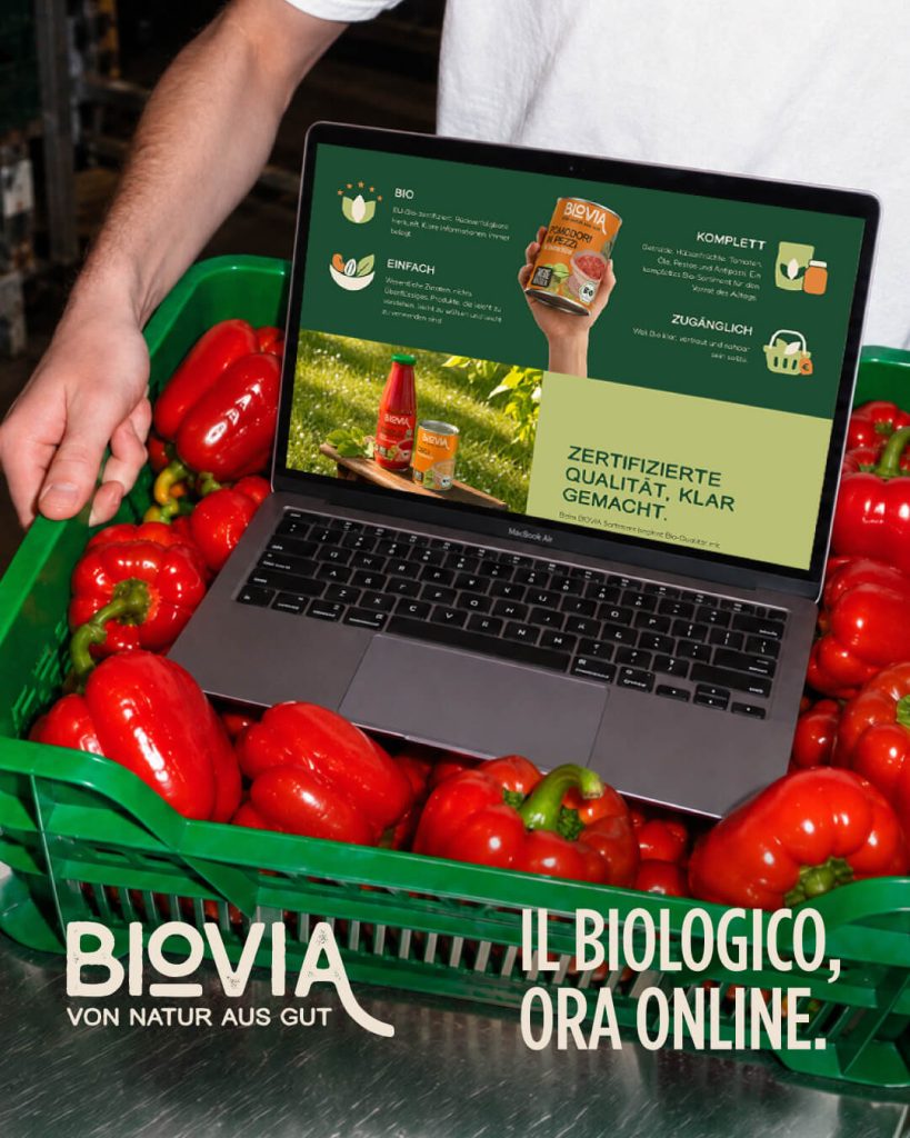 bioviafood.de on a laptop in a crate of red peppers, with BIOVIA logo and the line «Organic, now online»
