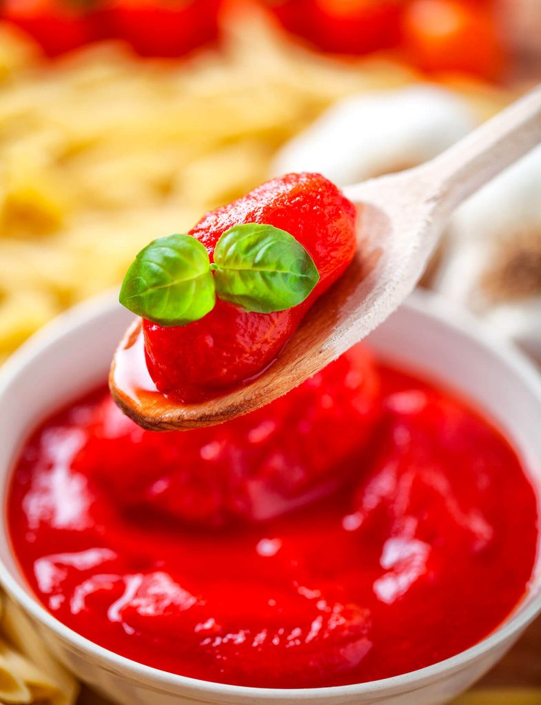 Pelati: pomodori pelati interi con foglie di basilico su cucchiaio sopra salsa di pomodoro