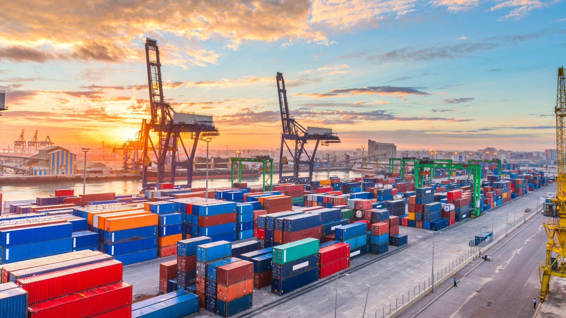 Aerial view of a busy international port with cranes and colourful containers at sunrise, symbolising global logistics and Atlante’s end-to-end supply chain model.